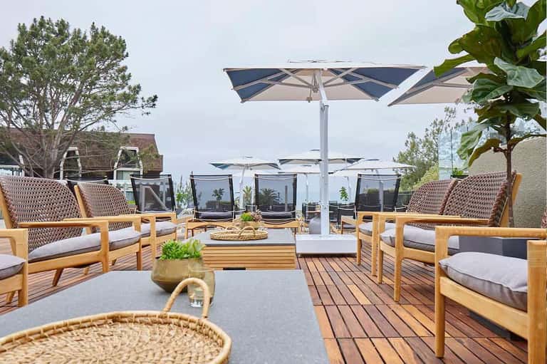 Resort rooftop lounge with wooden chairs, umbrellas, and city views.