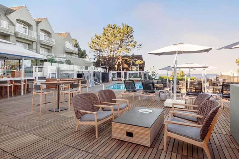 Oceanfront resort terrace with lounge seating, umbrellas, pool and water views at sunset