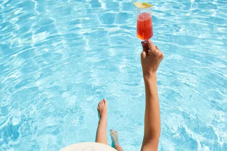 Person in pool holding red tropical cocktail with lime garnish