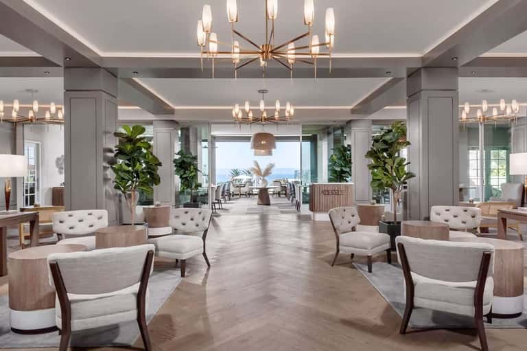 Elegant hotel lobby with marble floors, modern chandeliers, potted plants, and ocean view through windows