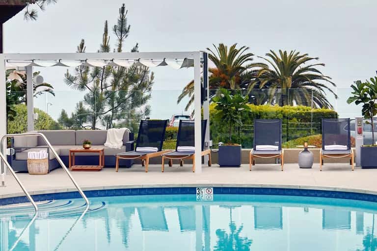 Upscale pool area with modern lounge seating, pergola shade structure, and palm trees