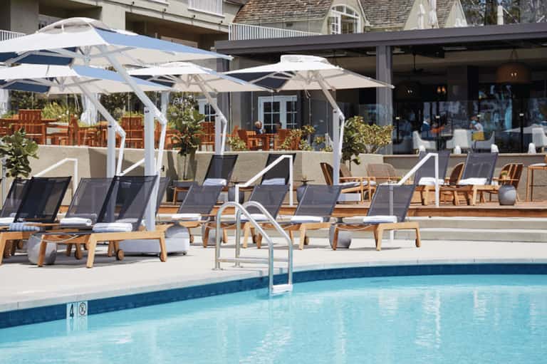 Resort pool deck with lounge chairs, white umbrellas, and oceanfront building