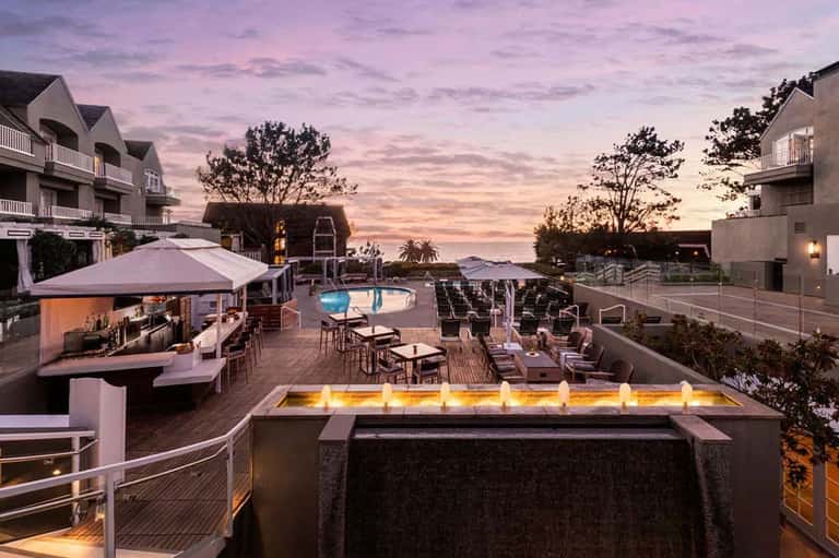 Resort terrace at dusk with fire pit, pool, lounge chairs, and ocean view