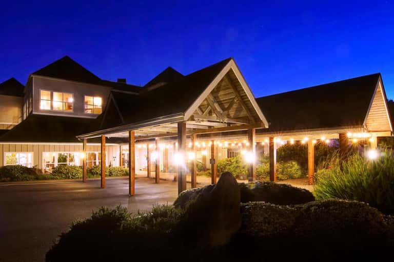 Upscale restaurant exterior lit at dusk with wooden beamed entry and large windows