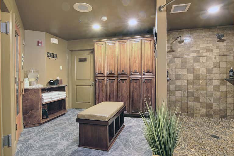 Spa locker room with wooden lockers, massage table, towel storage, and large tiled shower area