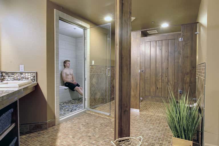 Large spa bathroom with two modern showers, glass enclosures, neutral tile flooring, vanity sink, and wood accents.