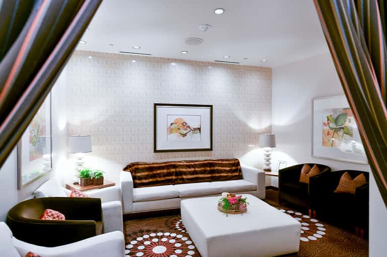 Elegant hotel lounge with white sofa, black chairs, patterned carpet, and botanical artwork on neutral walls