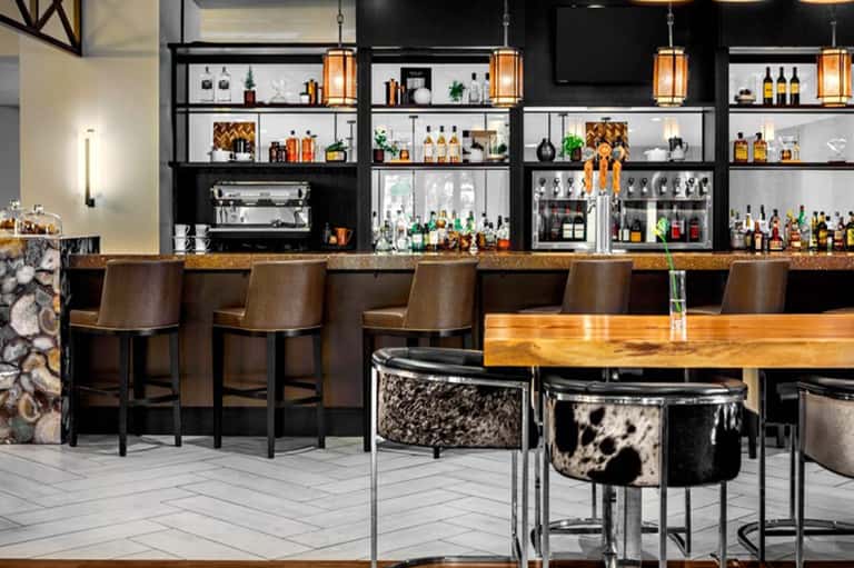 Modern bar with black and white shelving displaying bottles, wood countertops, and cow-print bar stools
