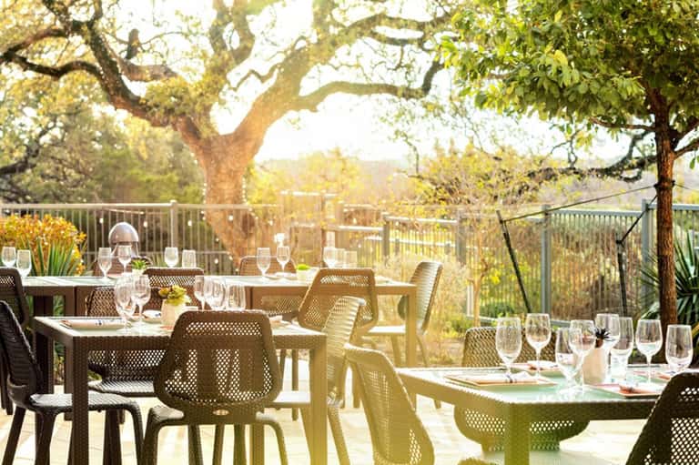 Outdoor dining terrace under large oak trees with place settings and views