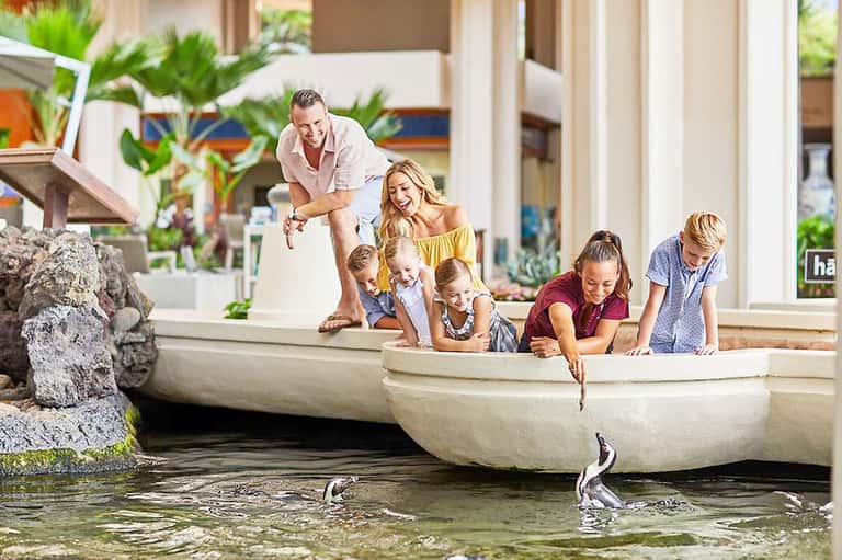 Family of five fishing from boat in resort's lagoon with tropical architecture backdrop