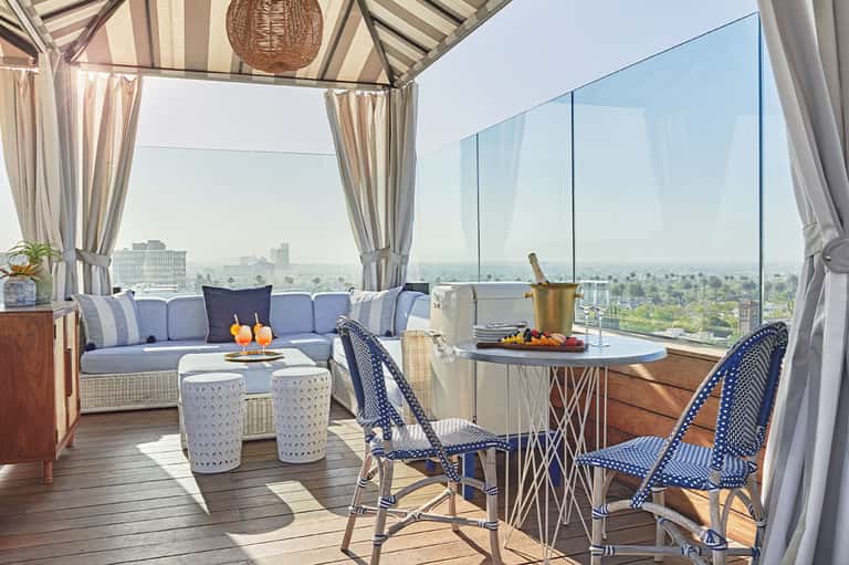 Luxury rooftop lounge with blue seating, striped awning, city skyline views, and champagne