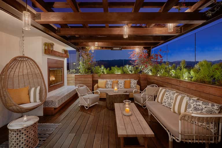 Modern rooftop lounge with wooden beams, hanging chairs, and mountain views at dusk
