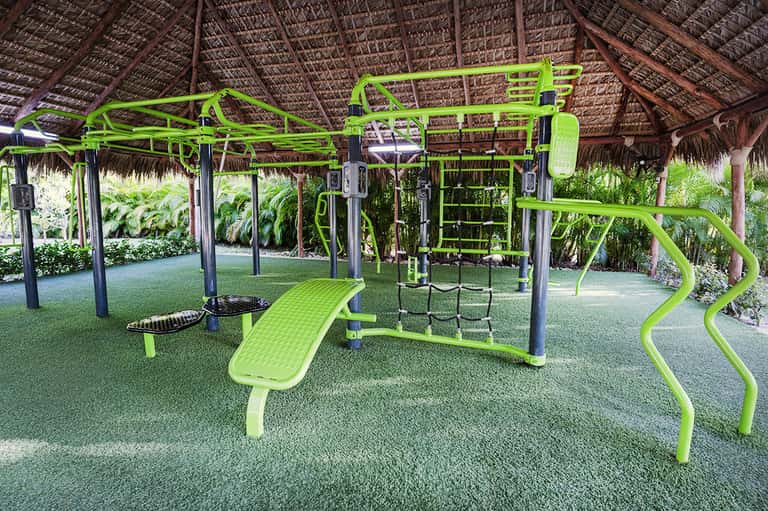 Bright green outdoor fitness equipment under thatched roof with tropical garden surroundings