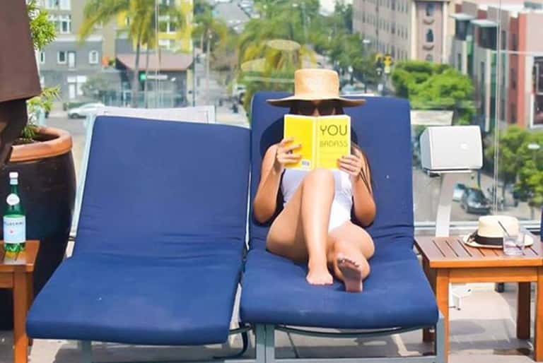 Woman reading on blue lounge chairs on a rooftop terrace overlooking a city skyline