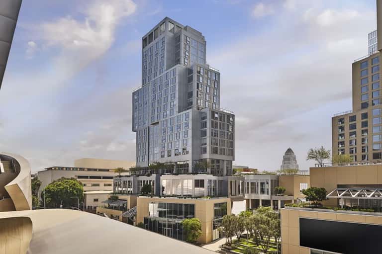 Modern mixed-use building with stepped architecture and landscaped rooftop among downtown buildings
