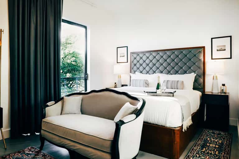 Elegant hotel bedroom with quilted headboard, dark drapes, and seating area
