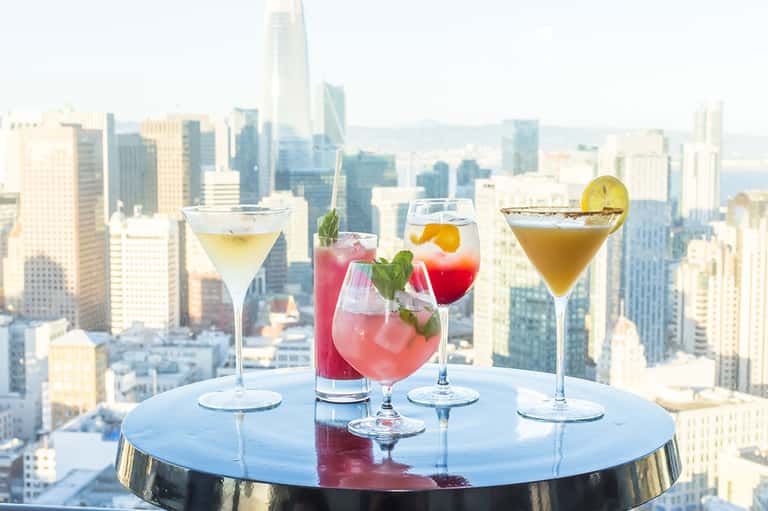 Four colorful cocktails on table with city skyline view from high-rise rooftop bar