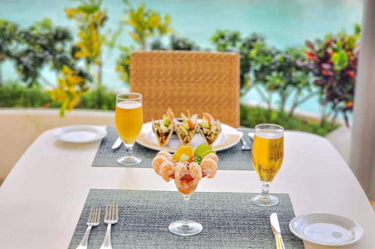 Outdoor dining table with appetizers, beer glasses, tacos, and ocean view background