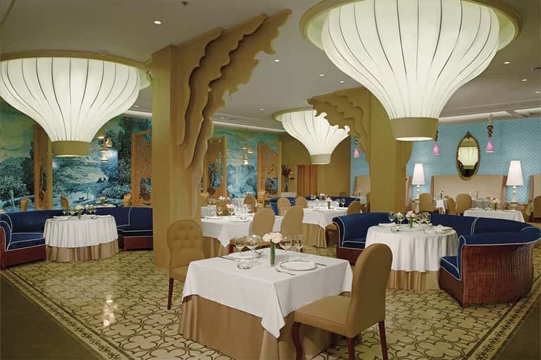 Elegant dining room with shell-shaped light fixtures, gold columns, and round white-draped tables