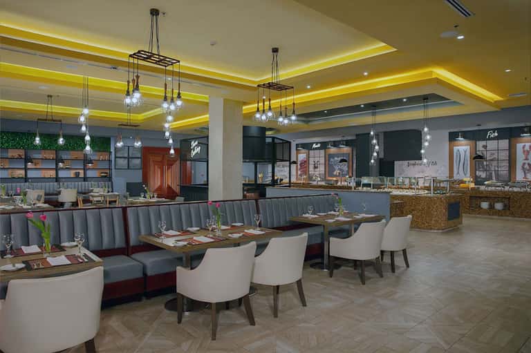 Restaurant dining area with yellow ceiling accent, hanging lights, gray banquettes, and modern furnishings