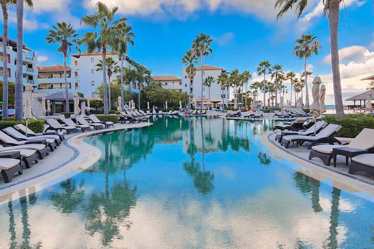 Lagoon-style pool with turquoise water, palm trees, white buildings, and black lounge chairs