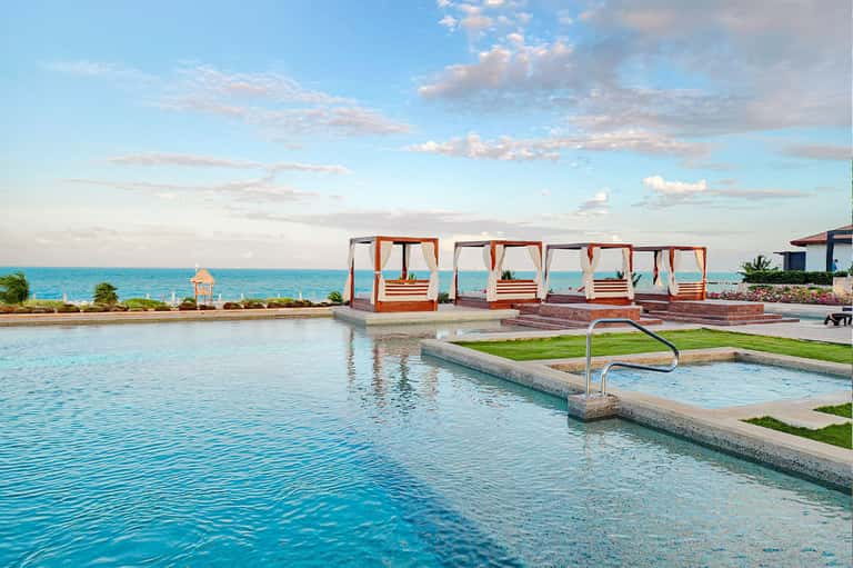 Luxury resort infinity pool overlooking turquoise ocean with cabanas and beach