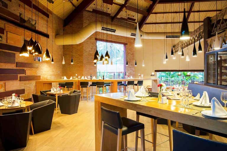 Modern restaurant interior with wood accents, pendant lighting, and large windows overlooking tropical grounds
