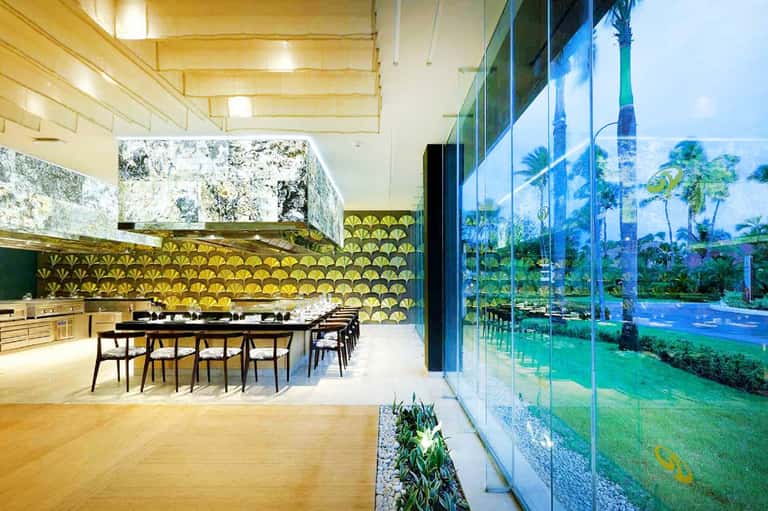 Modern kitchen with yellow patterned backsplash, white counters, and floor-to-ceiling windows overlooking tropical landscape