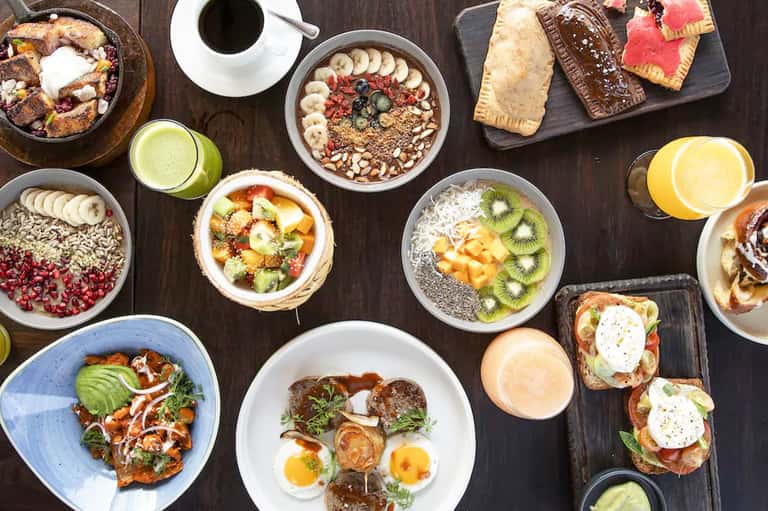 Colorful overhead view of breakfast spread with smoothie bowls, fresh fruit, and pastries