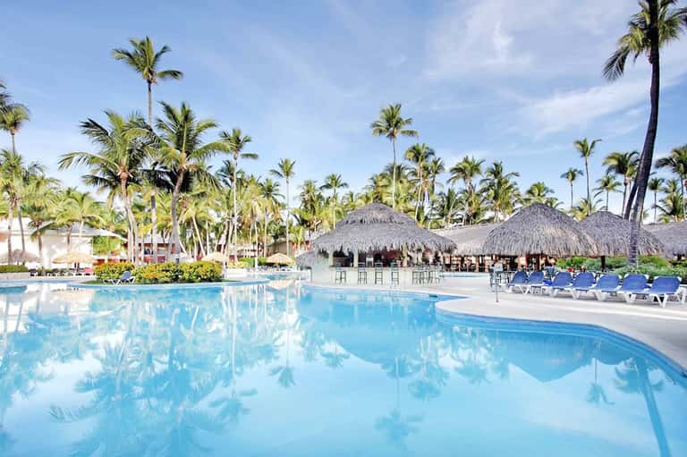 Large lagoon-style pool with palm trees, tiki bars, and lounge chairs at tropical resort