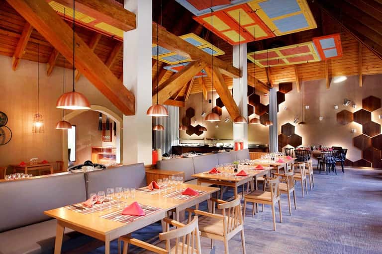 Modern restaurant interior with exposed wooden beams, copper pendant lights, white walls, and set dining tables