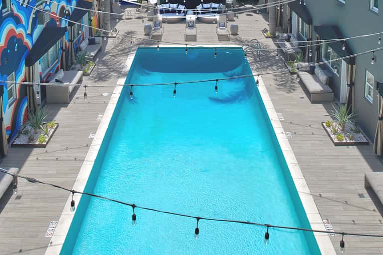 Lap pool viewed from above with bright blue water, wooden deck, lounge chairs, and colorful wall art