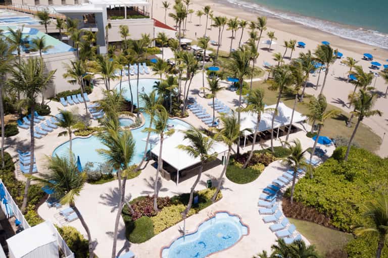 Aerial view of beachfront resort with multiple pools, palm trees, beach, and ocean