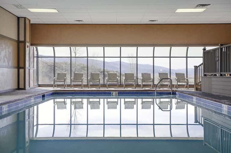 Indoor lap pool with large windows overlooking mountains and lounge chairs along the deck