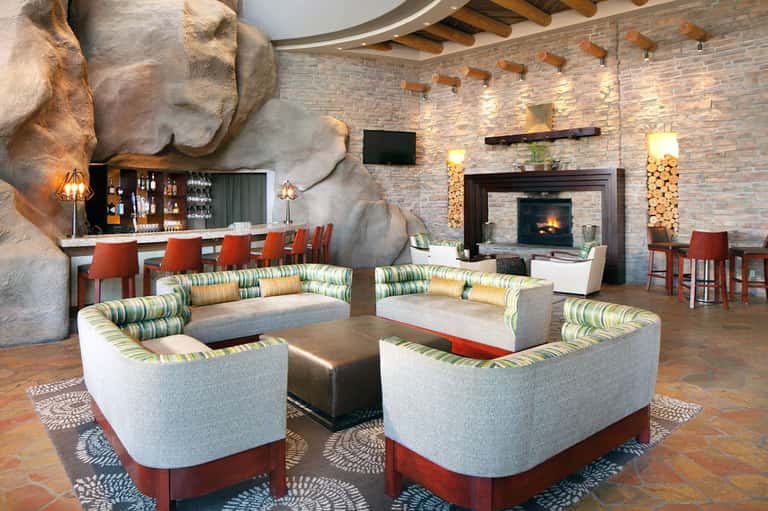 Modern hotel lounge with dramatic rock accent wall, fireplace, striped seating, and bar area