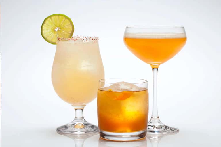 Three cocktails on white background: margarita, whiskey, and tropical drink