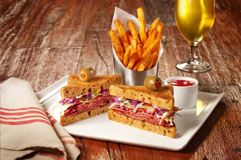 Gourmet sandwich with fries and white wine on wooden table with striped napkin