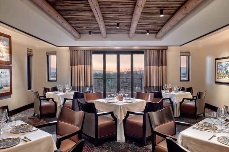 Elegant dining room with white tablecloths, exposed beams, and panoramic windows at dusk