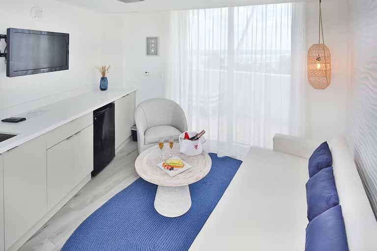 Modern resort suite with kitchenette, white furnishings, and ocean view