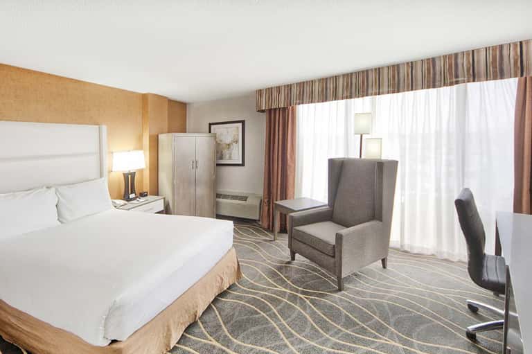 Hotel room with white bedding, gold accent wall, sitting area with windows, and modern décor