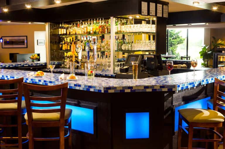 Modern bar with blue tile countertop, extensive liquor selection, and ambient lighting
