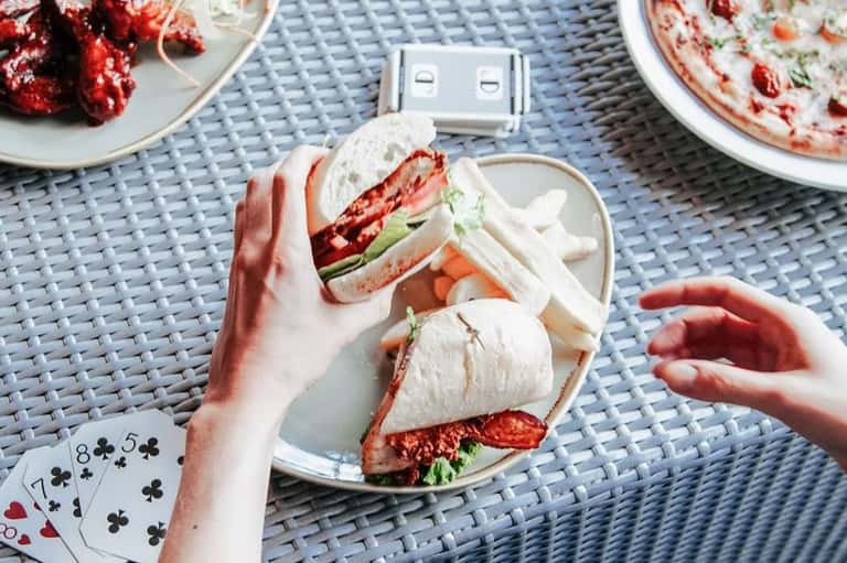 Hands holding fresh lobster sandwiches at poolside table