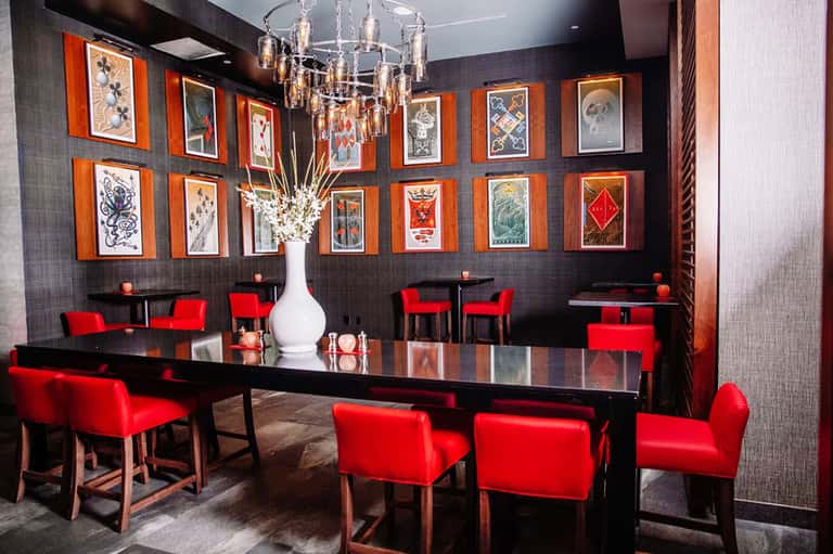 Upscale dining room with black walls, orange-framed artwork, and red chairs
