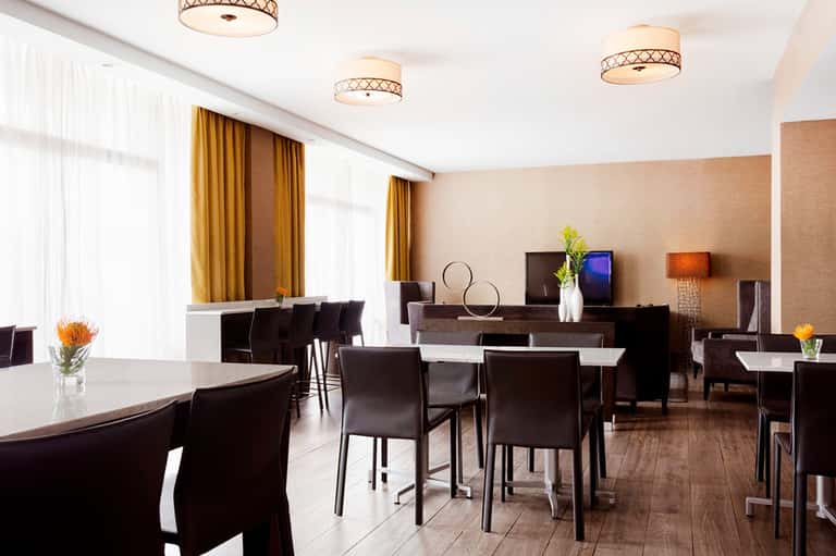 Elegant hotel event space with round dining tables, black chairs, warm lighting, and contemporary décor