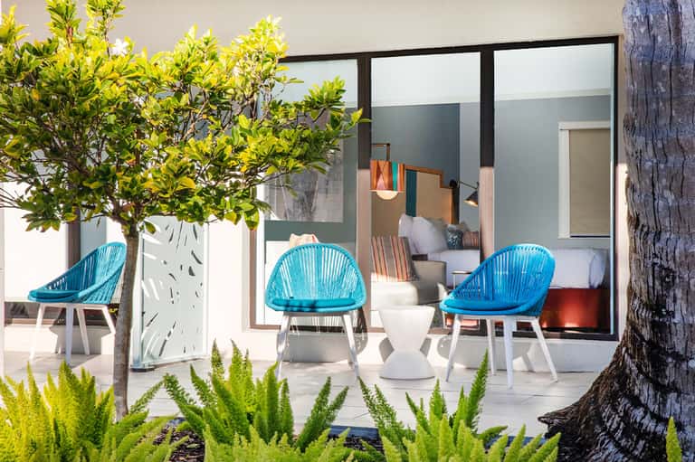 Modern outdoor patio with turquoise woven chairs, potted plants, and floor-to-ceiling glass doors