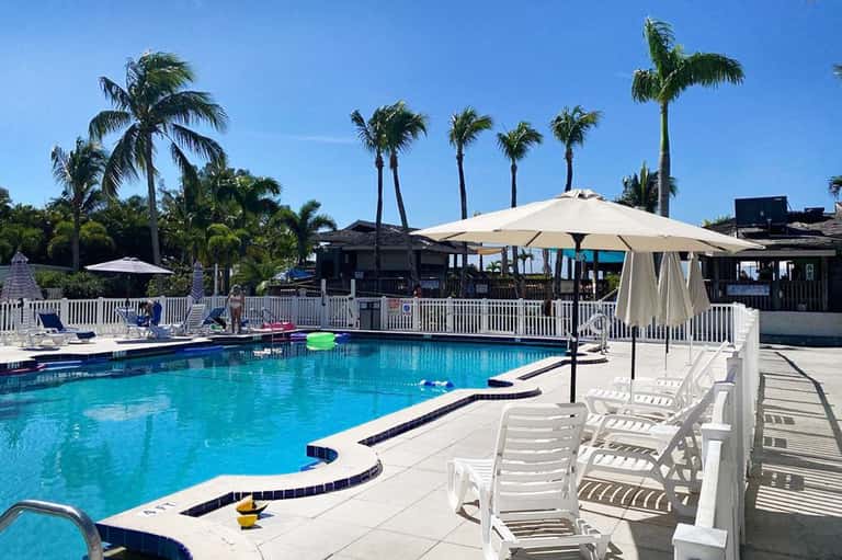 Resort pool with turquoise water, white umbrellas, palm trees, and beachfront pavilions