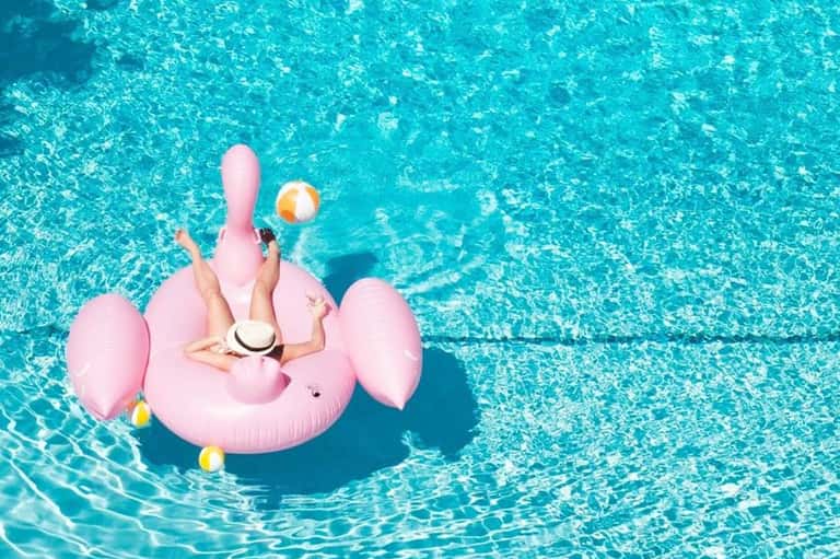 Woman on pink flamingo float in crystal-clear turquoise pool water with beach ball