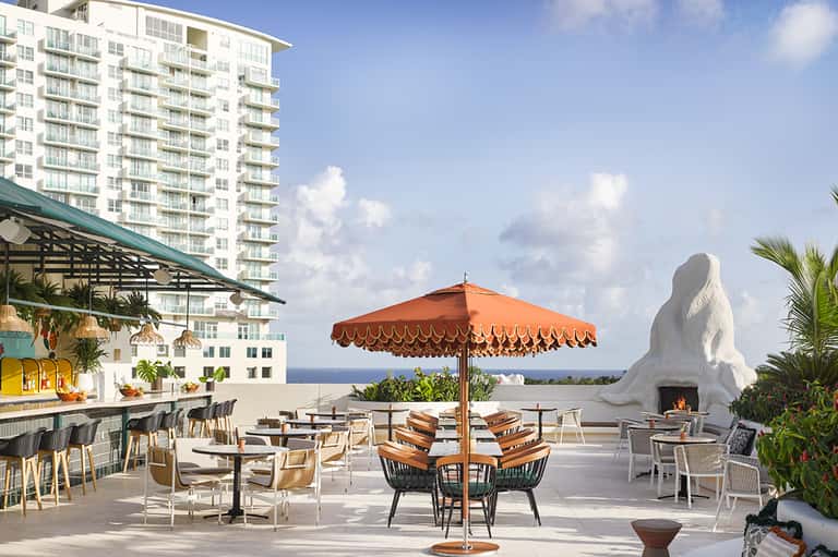 Beachfront resort terrace with orange umbrella, fire pit, and ocean view with modern architecture.