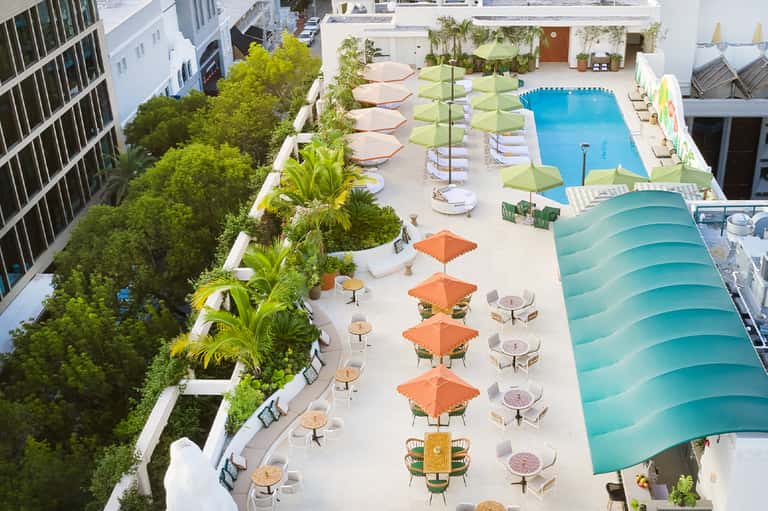 Aerial view of resort pool deck with green umbrellas, lounge chairs, and surrounding buildings