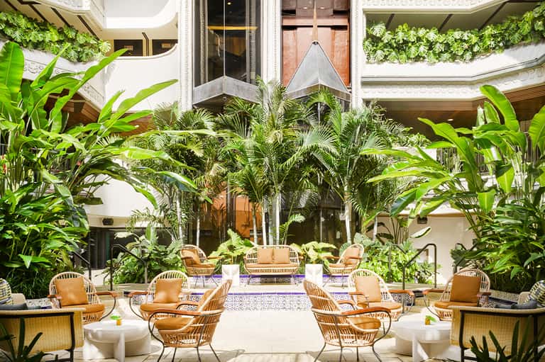 Elegant indoor courtyard with tropical plants, wrapped ceiling details, and rattan seating